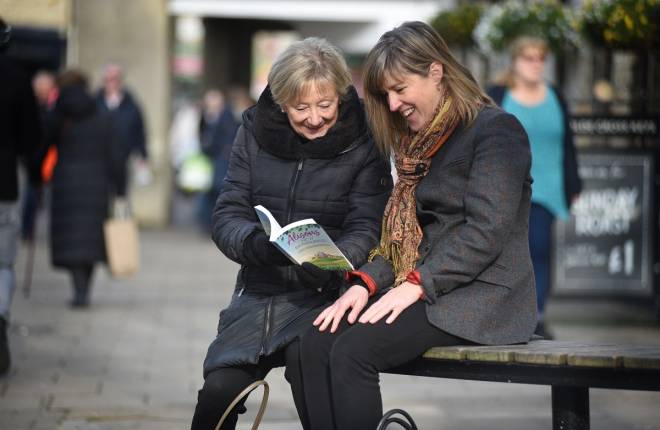 Two women sitting outside reading a book
