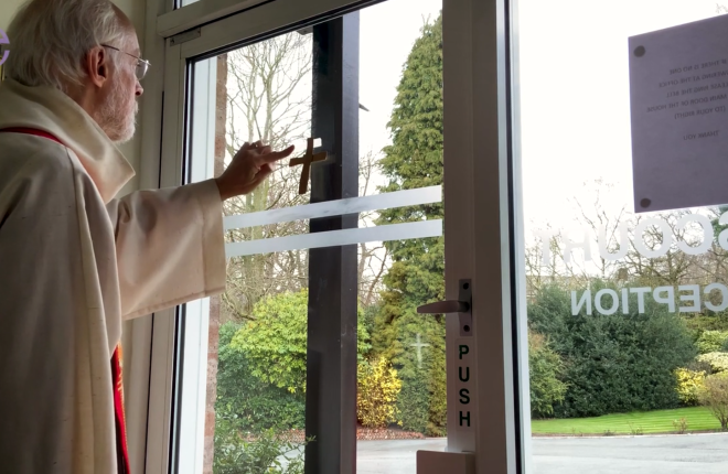The Bishop of Manchester sticking a Palm Sunday cross up in his window at home.