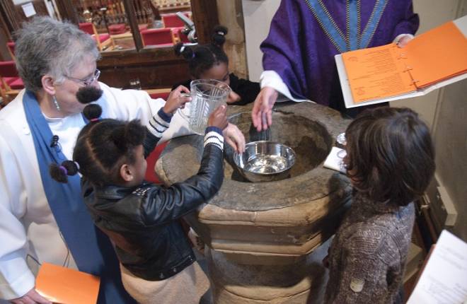 Children help the vicar pour water into the font
